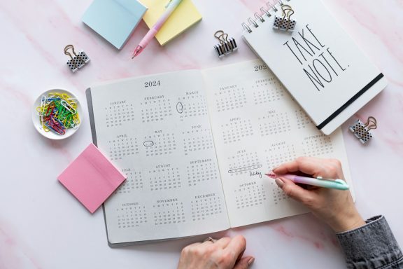 Main notebook with a calendar, sticky notes, and colorful paper clips on a marble surface.